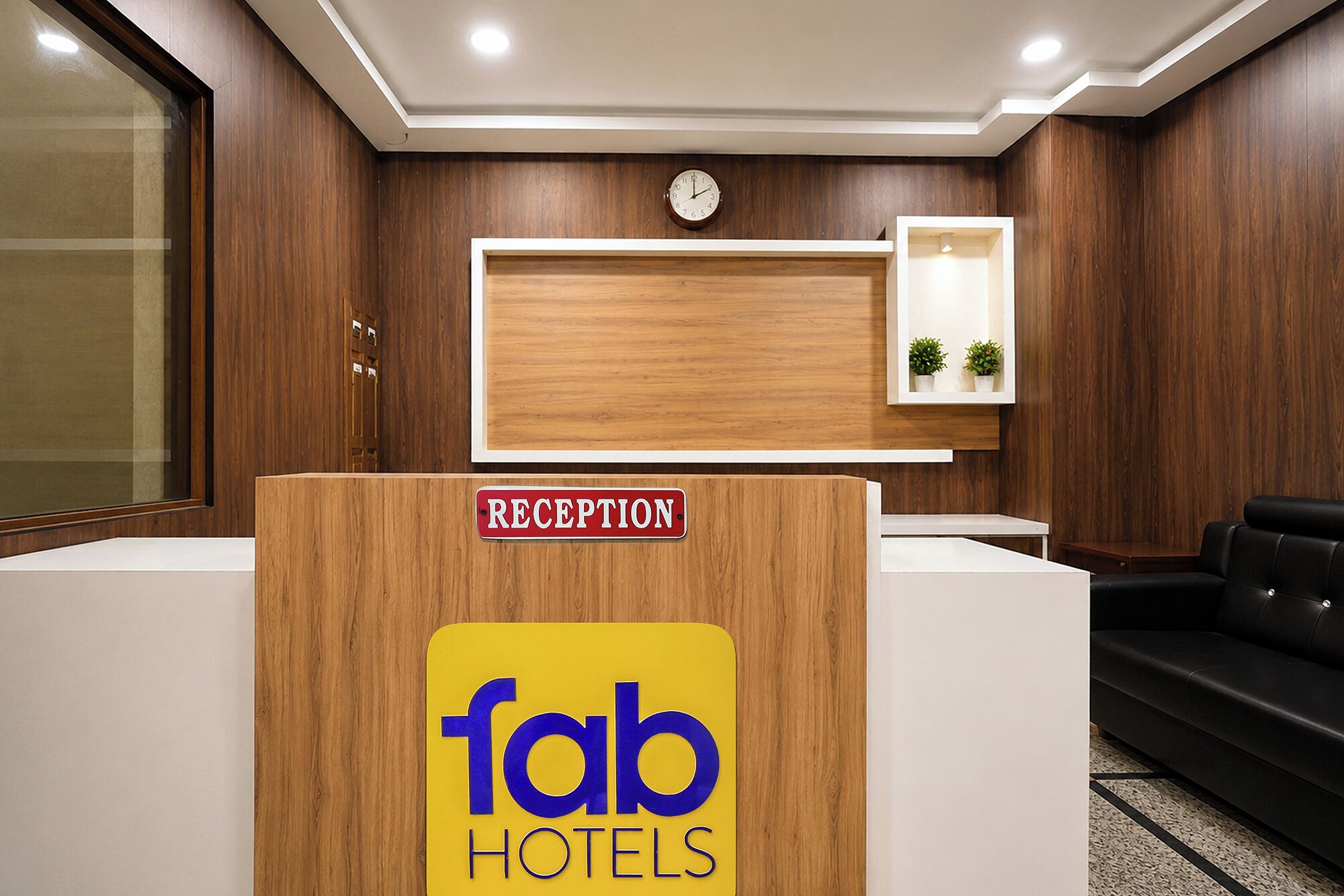 Uma receção com o letreiro 'fab hotels', um relógio e um pequeno arranjo de plantas.