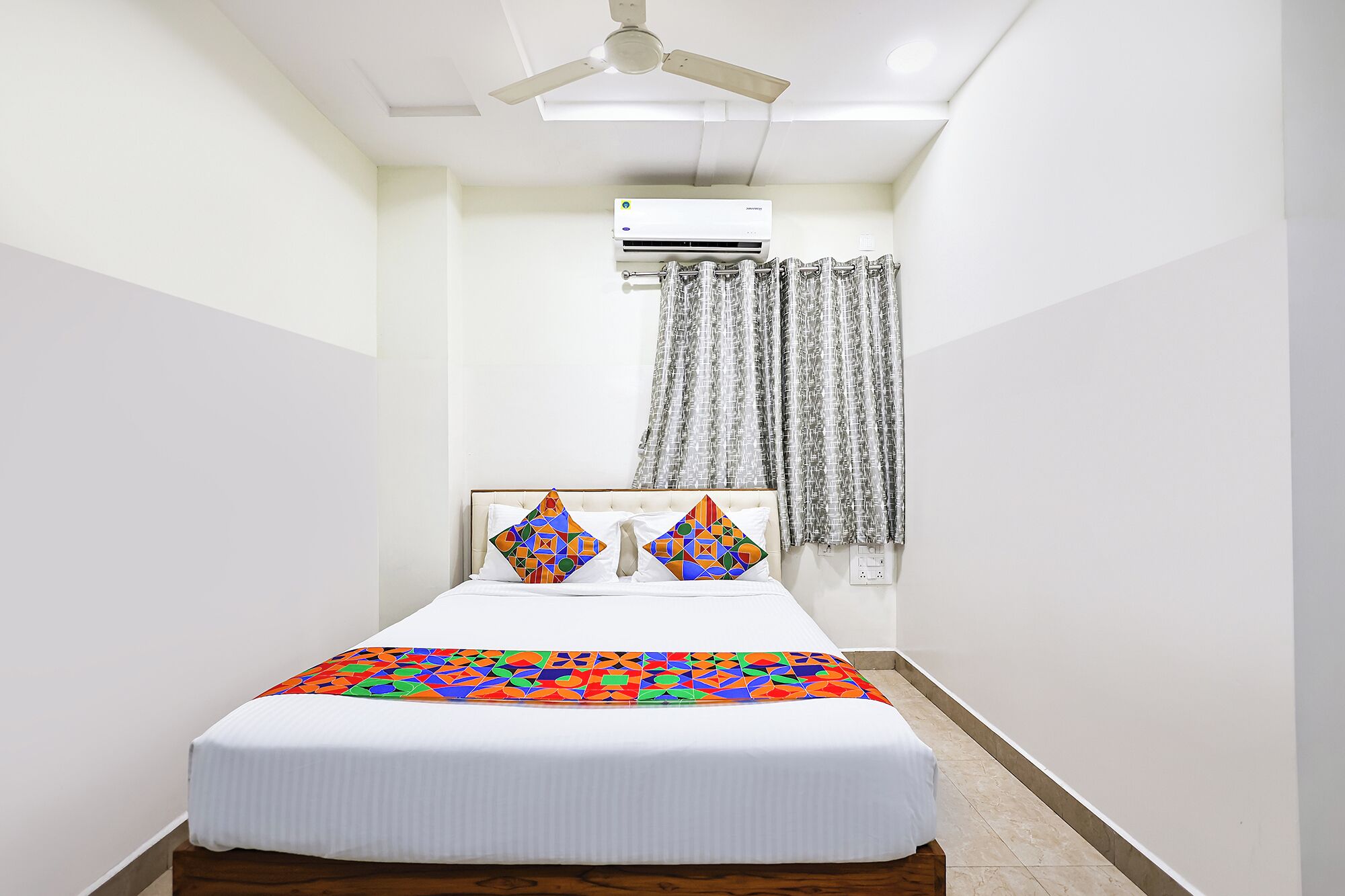 Ein Hotelzimmer mit einem Bett, einem Deckenventilator, einer Klimaanlage und einem mit Vorhängen versehenen Fenster.