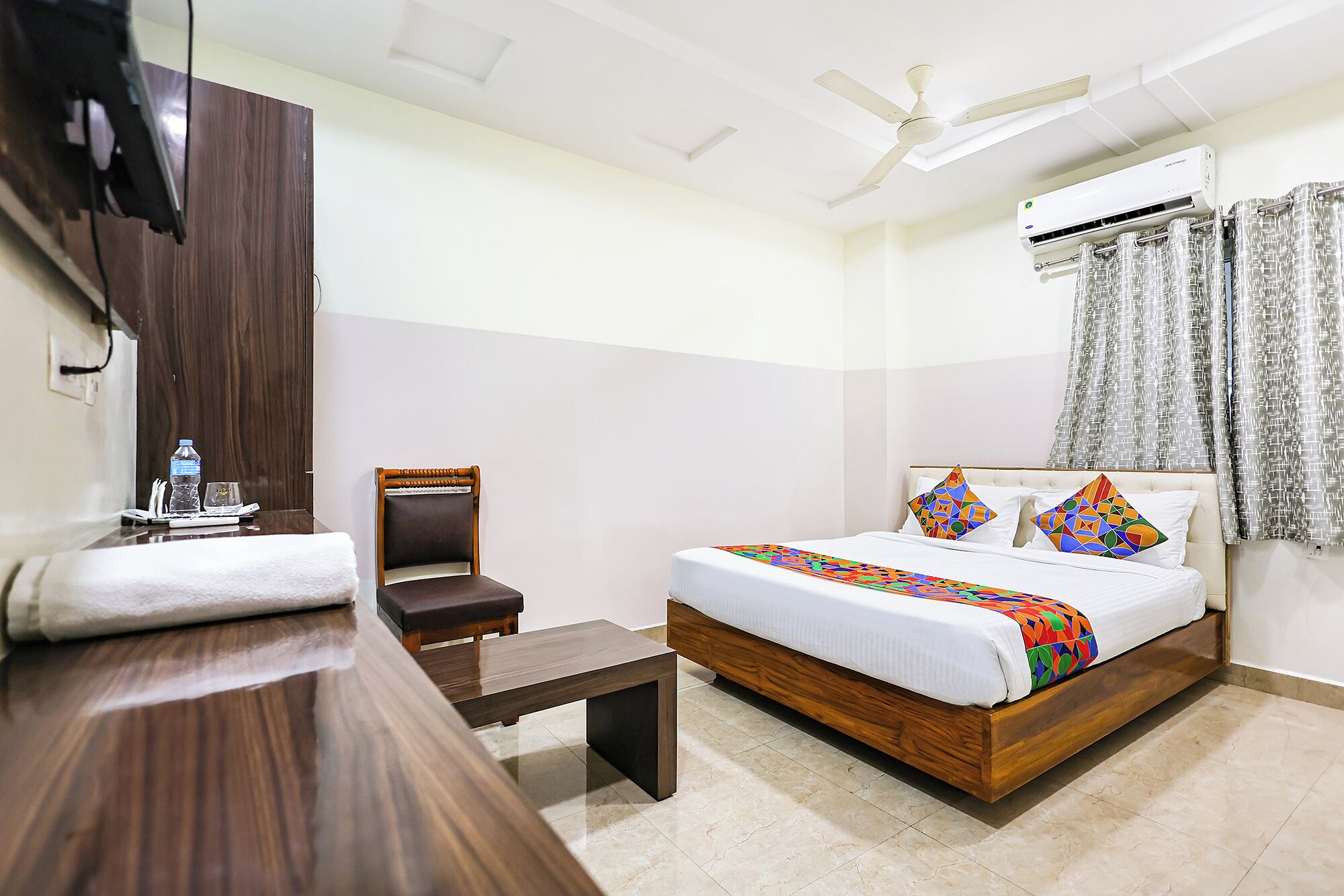 Hotelkamer met een bed, een stoel, een bureau, een airconditioner en een plafondventilator.