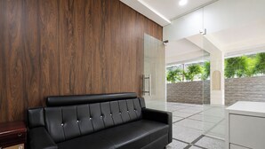 Un área de recepción moderna con un sofá de cuero negro, un panel de pared de madera y una puerta de cristal que da a un espacio exterior.