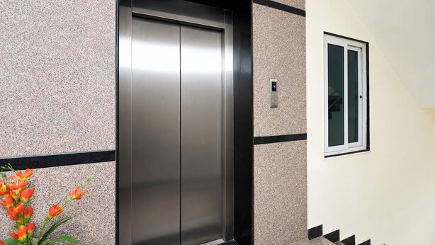 An elevator with a metallic finish, a small window with a black frame, and a wall with a textured pattern. - FabHotel Anu Grand - Vijayawada (Vijayawada)