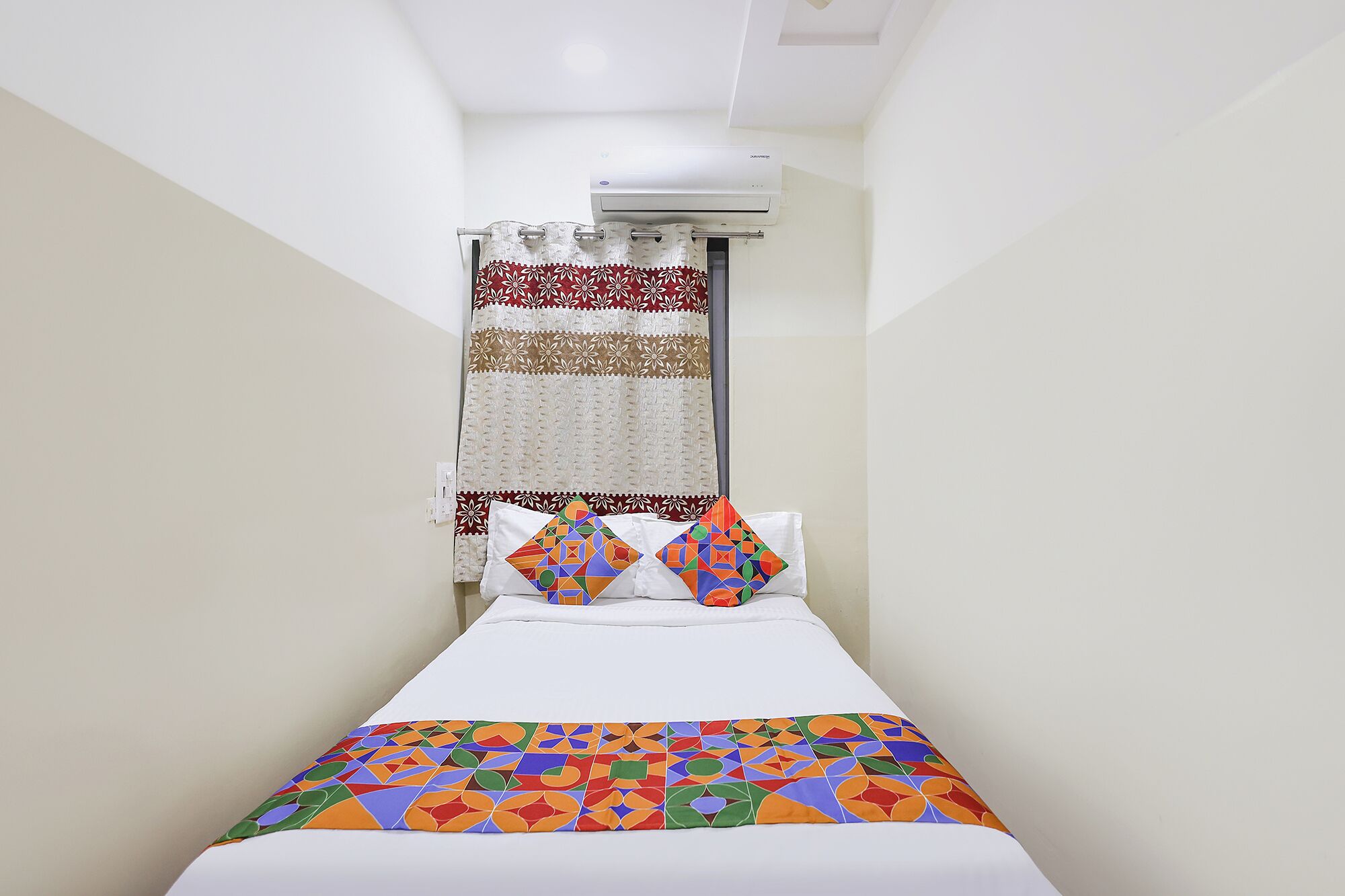 Ein schmales Hotelzimmer mit Bett, einem gemusterten Vorhang und einer Klimaanlage.