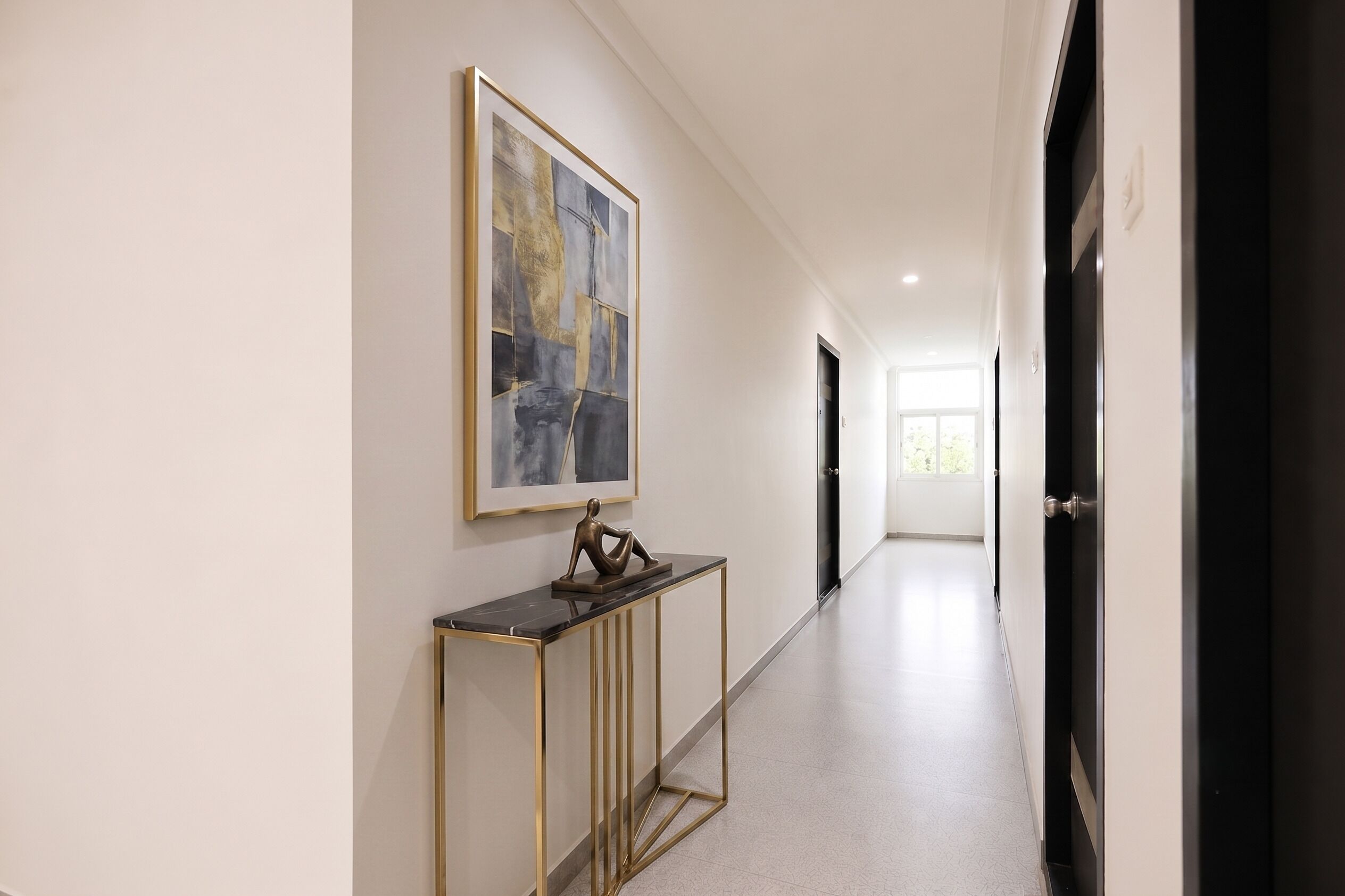 A hallway with a framed abstract painting, a small sculpture on a console table, and a door at the end.