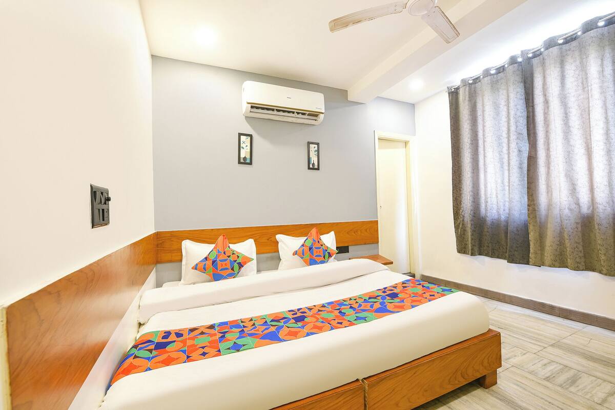 Habitación de hotel con cama, aire acondicionado, ventana con cortinas y ventilador de techo.