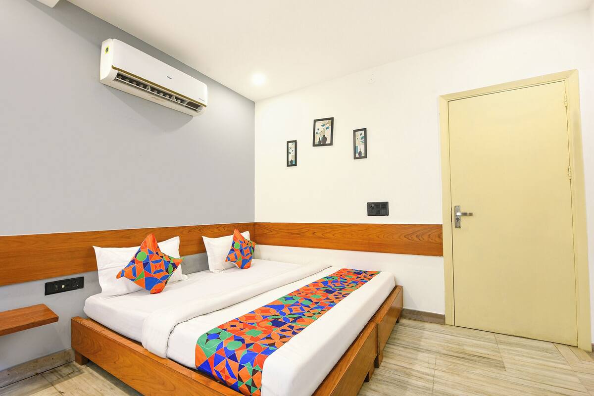 Una habitación de hotel con una cama, cabecera de madera, una puerta y un equipo de aire acondicionado en la pared.