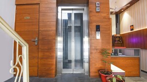An elevator with a wooden panel design, a sign indicating a toilet, and a reception desk with a potted plant. - Fabhotel Amar Residency (New Delhi)