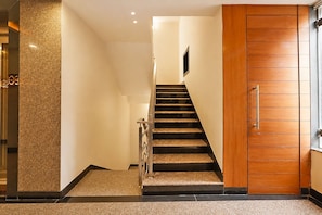 A staircase leading to a door with a wooden finish, a textured wall on the left, and a metal handrail. - Fabhotel Pratibha Grand (Vijayawada)