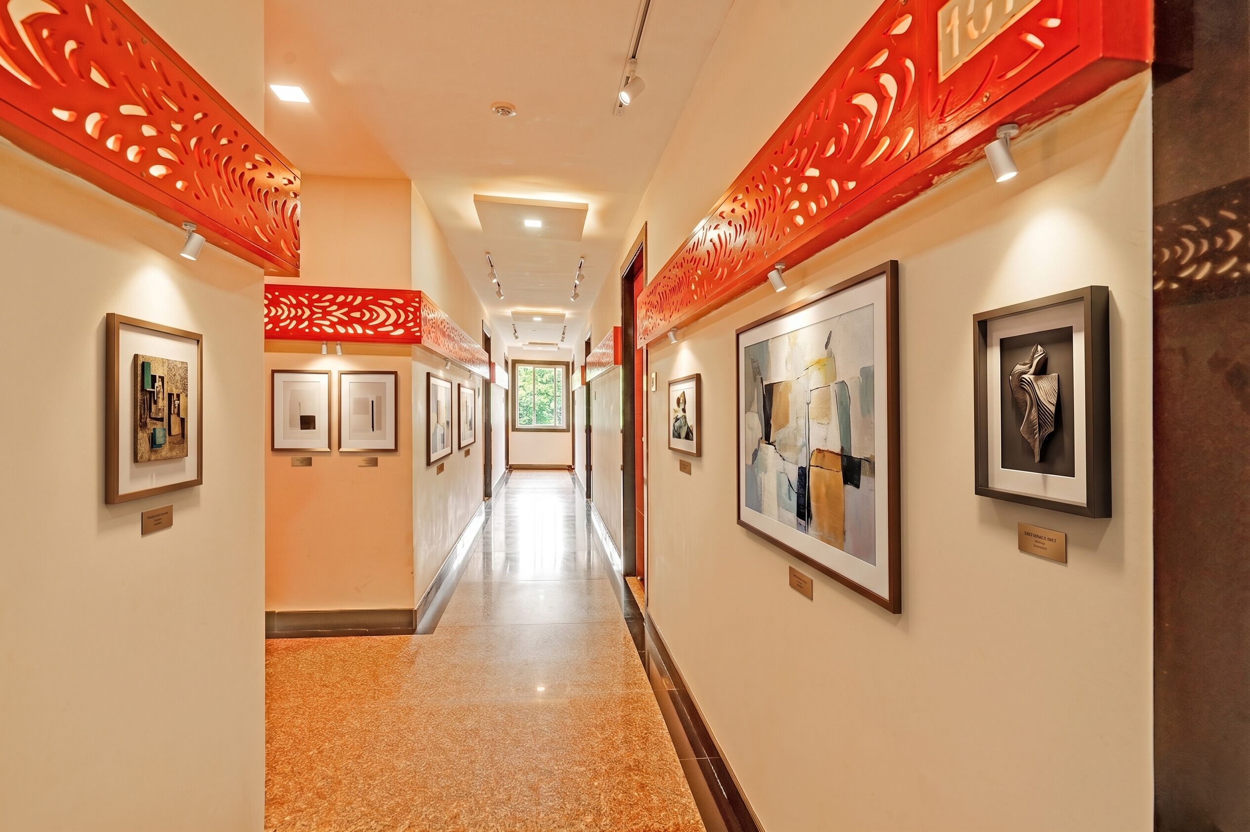 A hallway with framed artwork on the walls, a red decorative panel, and a polished floor.