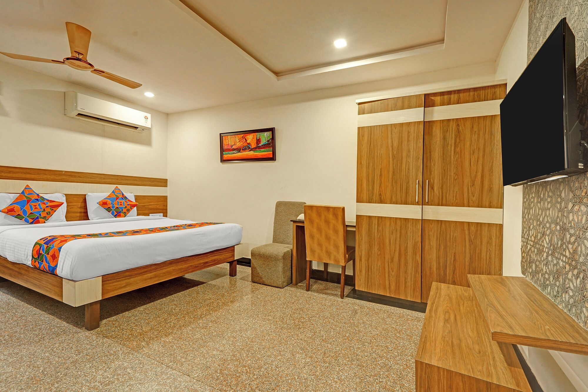 Una habitación de hotel con cama, escritorio, silla, televisor y ventilador de techo.