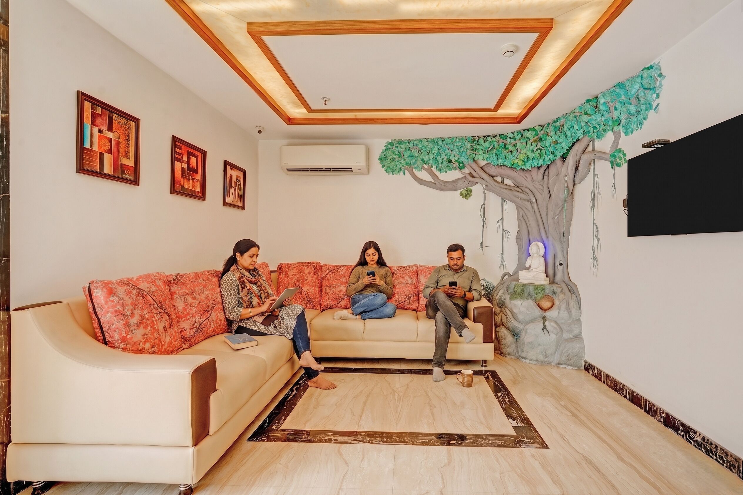 A living room with a sofa, a decorative tree, and framed artwork on the wall.