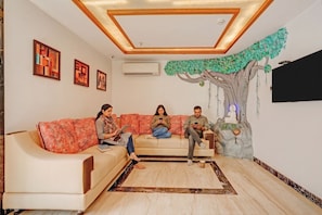 Una sala de estar con un sofá, una planta decorativa y cuadros en la pared.