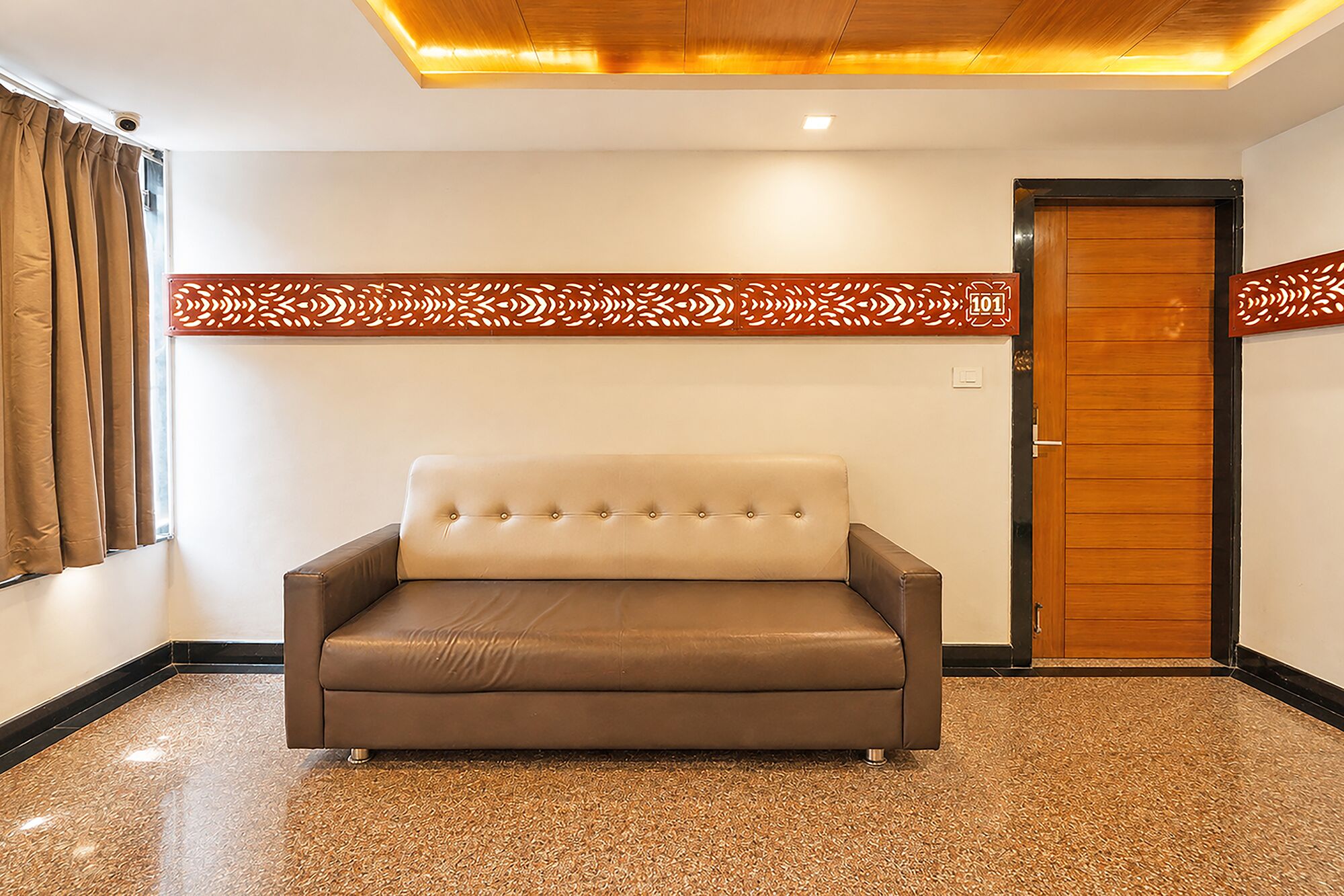 A room with a brown leather sofa, a wooden door, and a patterned wall decoration.