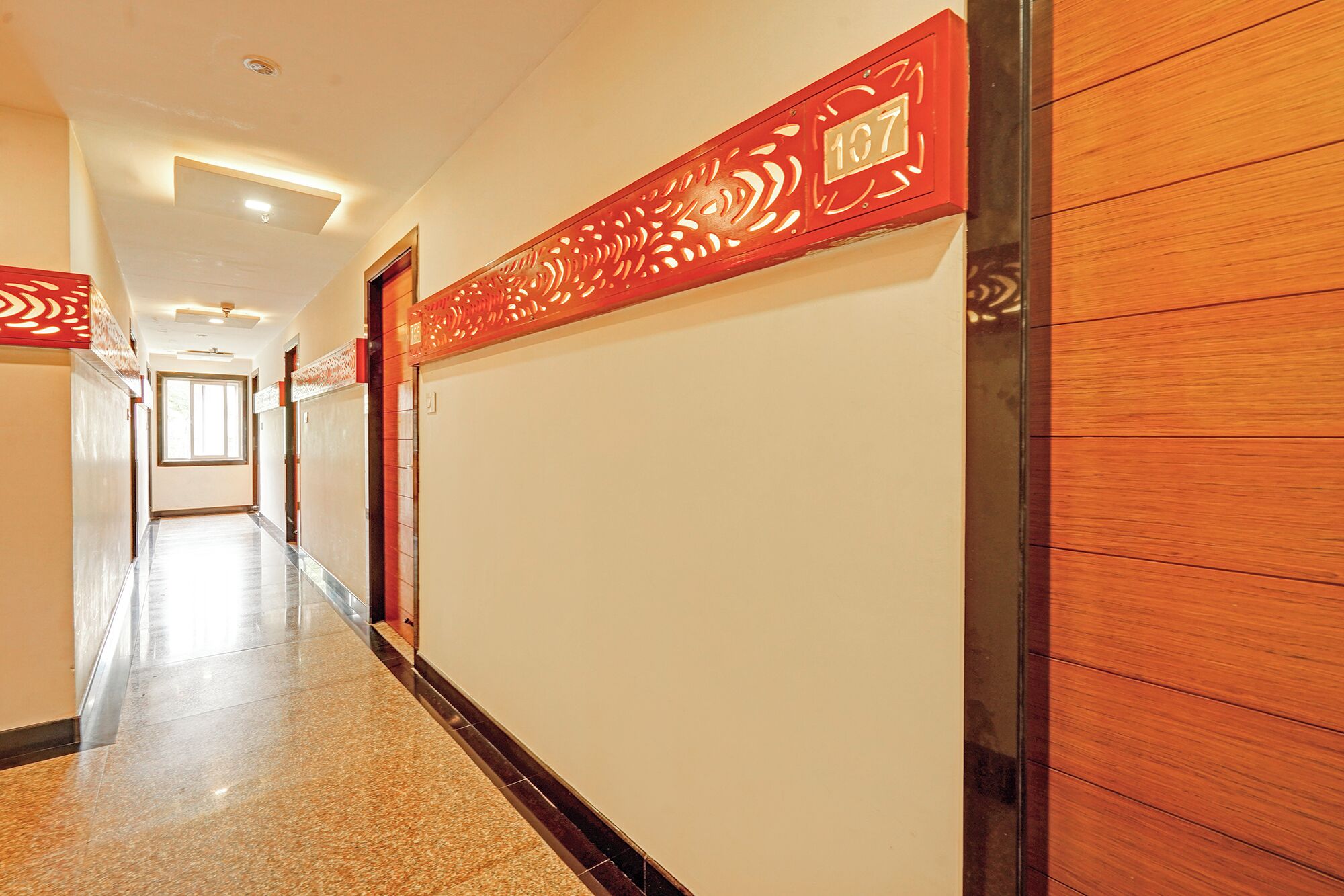 Un pasillo de hotel con una larga galería, paneles de madera y un letrero decorativo rojo con el número 107.