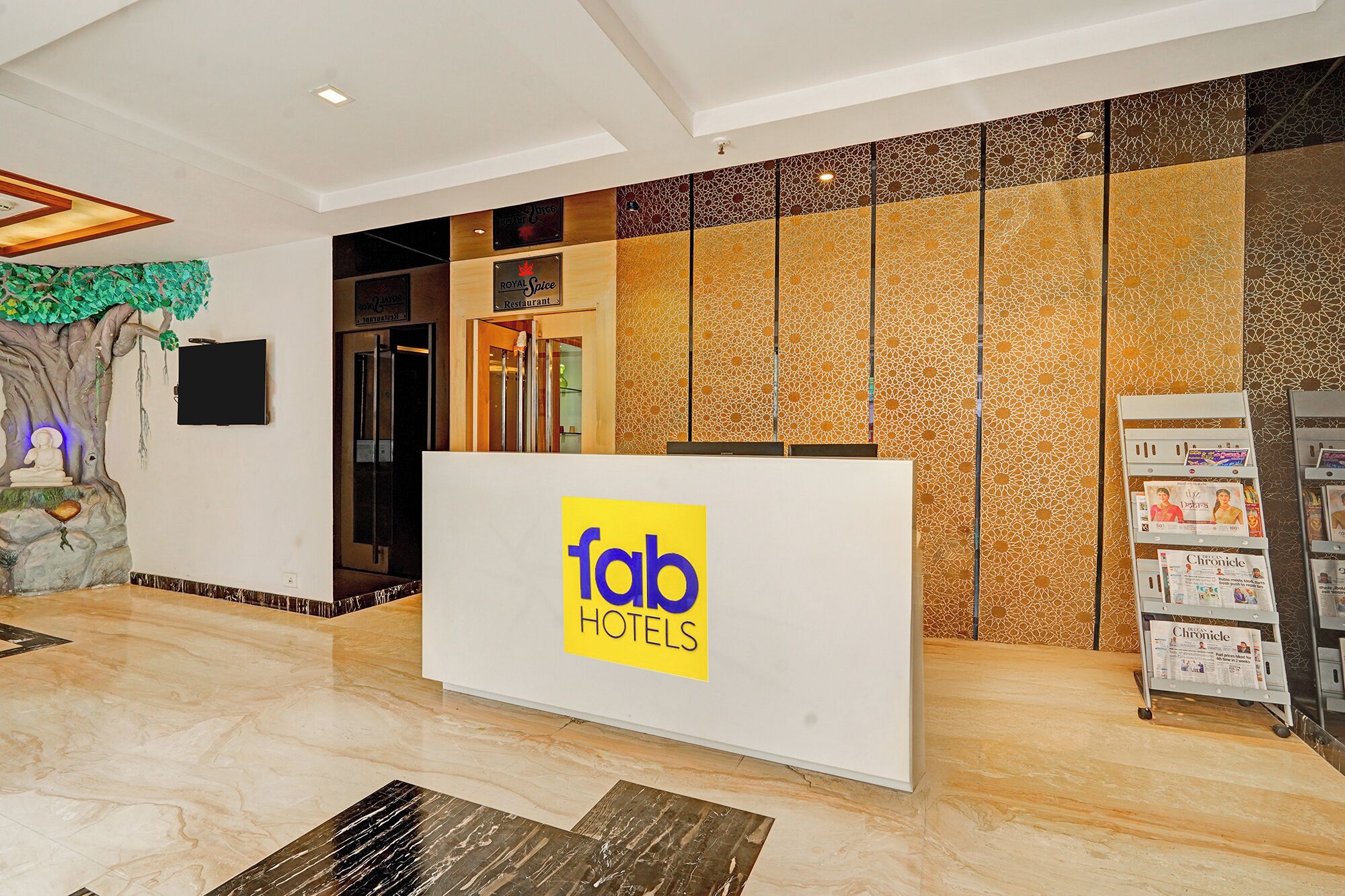 Een receptiebalie met een bordje 'fab HOTELS' in een moderne lobby met een boomsculptuur en een tijdschriftenrek.
