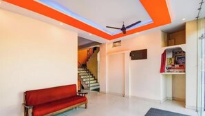 A room with a red sofa, a ceiling fan, a staircase, and a small shelf with items. - Fabhotel Radhy Stay (Jaipur)