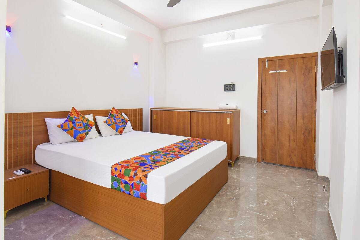 A hotel room with a wooden bed, a nightstand, a wardrobe, and a TV mounted on the wall.