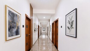 Um corredor com obras de arte emolduradas nas paredes, portas de madeira e chão de mármore.