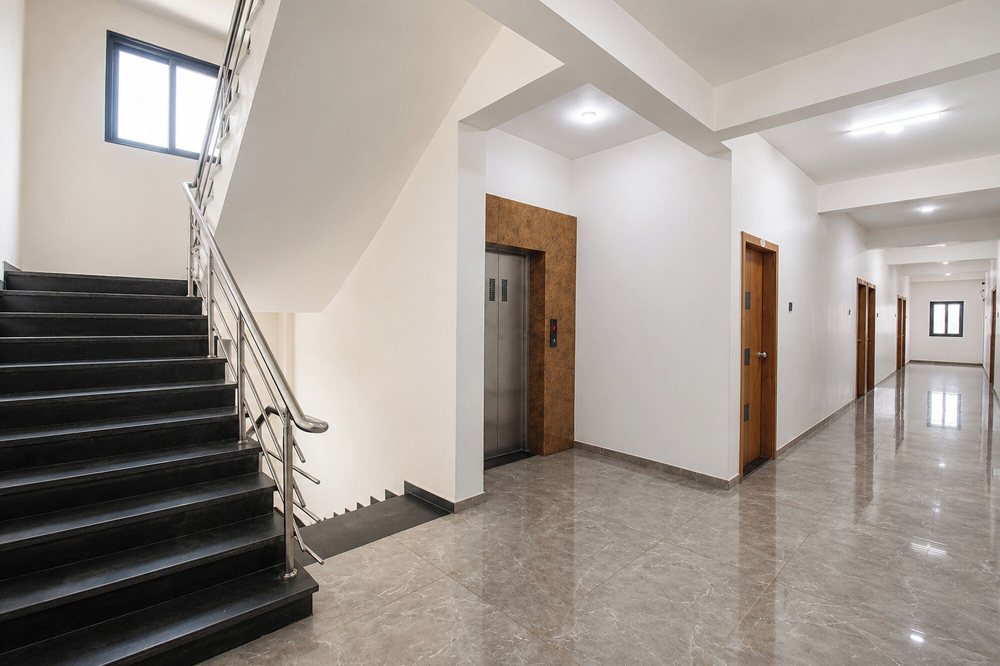 Een modern interieur met een trap, lift en een lange gang.
