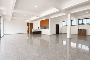 Interior espaçoso e moderno, com piso de mármore, área de cozinha com armários de madeira e grandes janelas que permitem entrada de luz natural.