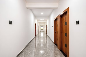 Un largo y estrecho pasillo con suelo de mármol pulido, paredes blancas y puertas de madera con detalles negros.