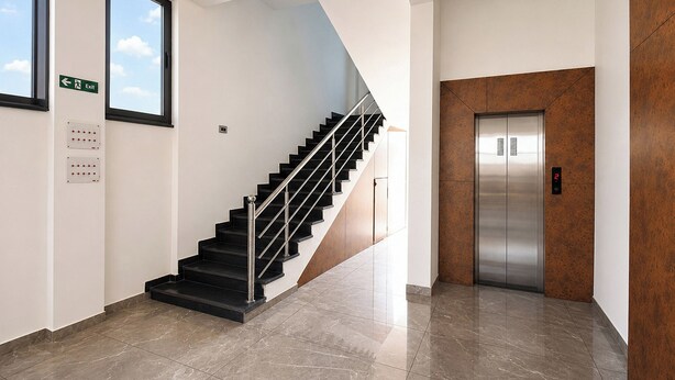 Um interior moderno com escada, elevador e céu azul visível por uma janela.
