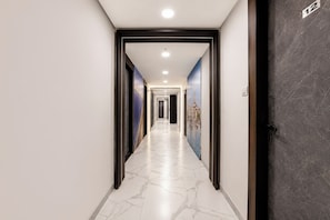 Un pasillo de hotel con piso de mármol, puertas con marco negro y un letrero con número en la pared.