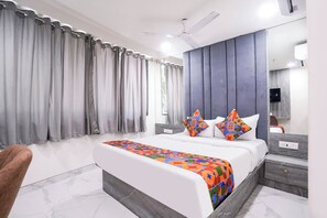 A modern bedroom with a bed, curtains, a ceiling fan, a bedside table, and a nightstand. - Fabhotel Byland International (Mumbai)