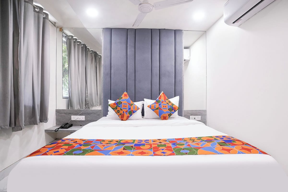 A modern hotel room with a bed, grey curtains, a ceiling fan, and an air conditioning unit.