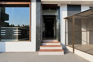 Ingresso di un edificio moderno con porta in vetro, cancello in metallo e una scalinata che conduce all'interno.