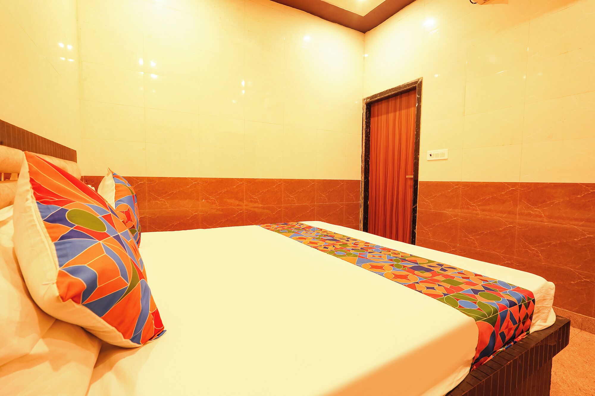 A hotel room with a bed, a door, and a light switch on the wall.
