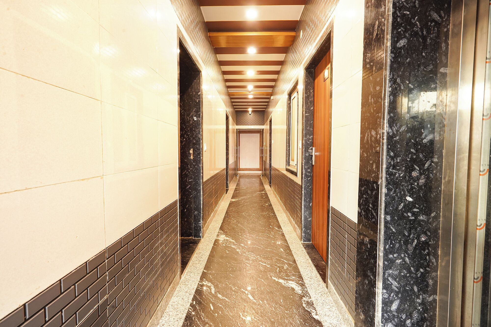 A long, narrow hallway with tiled walls, a marble floor, and wooden paneling on the ceiling.