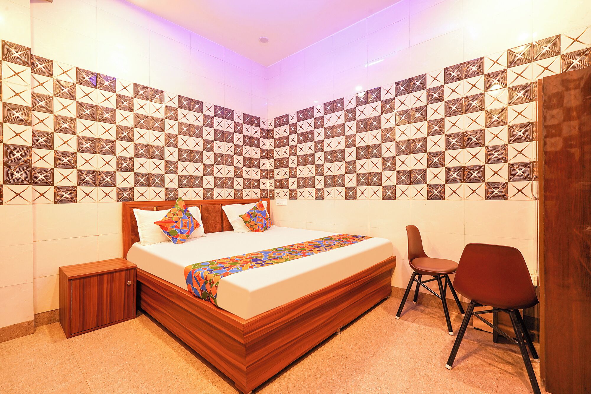 Una camera d'hotel con un letto, un comodino in legno, una sedia e pareti decorate con motivi.