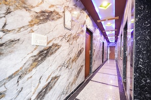 Un corridoio con rivestimento in marmo, illuminazione a incasso, una porta con il simbolo del numero e una presa di corrente.