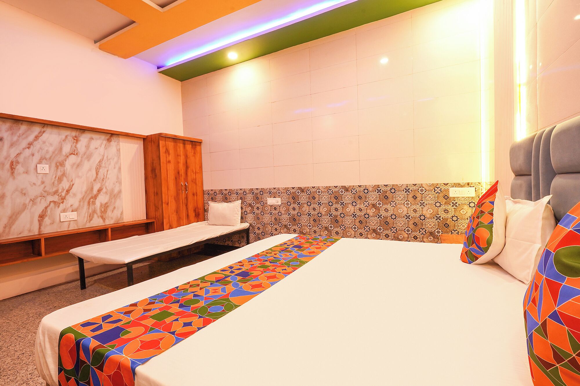 A hotel room with a bed, a bench, a wardrobe, and a patterned wall.