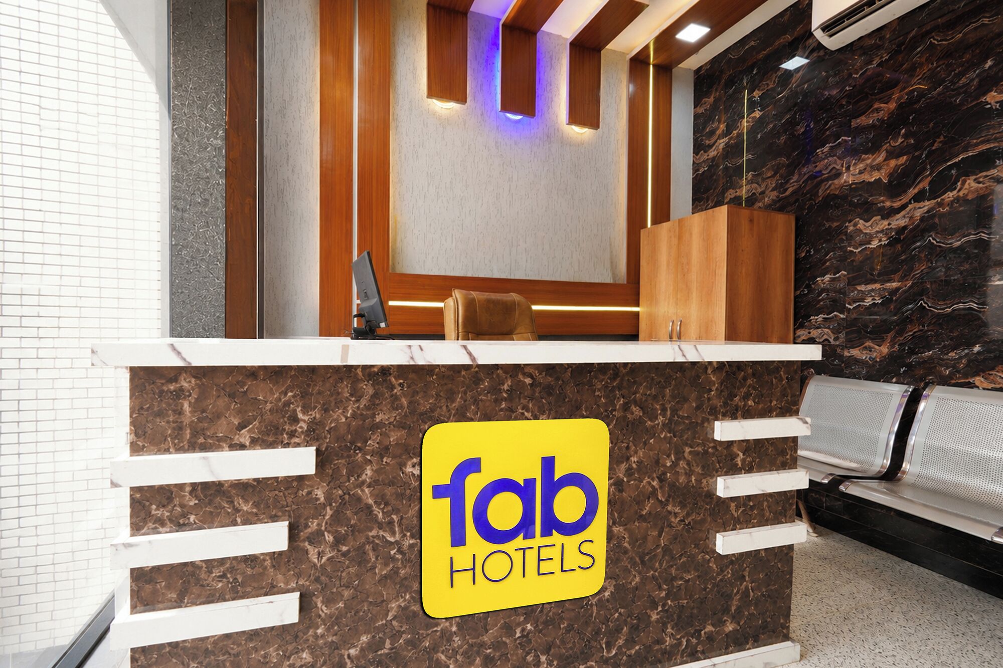 Ein Hotelrezeptionsschalter mit Marmorplatte, eine Sitzecke mit einer Bank und ein Schalter mit dem Schild 'fab hotels'.