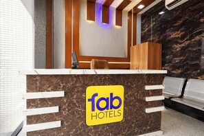 Una reception di hotel con un bancone in marmo, un'area salotto con una panca e una scrivania della reception con un cartello che riporta 'fab hotels'.