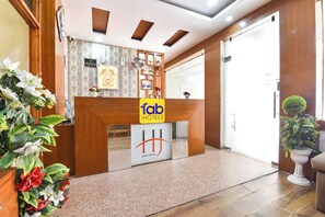 A hotel reception area with a wooden reception desk, a check-in counter, and a potted plant.