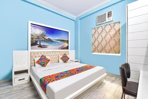 Une chambre à coucher comprenant un lit, une table de chevet, une chaise, un tableau représentant une scène de plage et une fenêtre avec des rideaux à motifs.