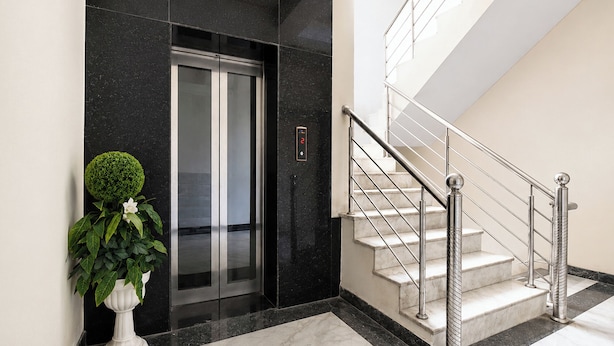 Een moderne lift met digitaal scherm, een trap met metalen leuningen en een potplant.