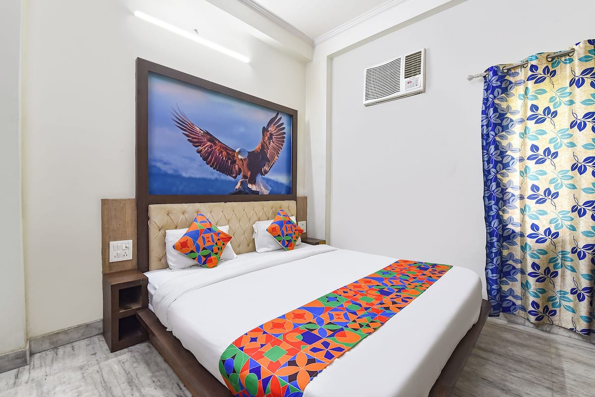 Une chambre dâhĂŽtel avec un lit, un grand tableau encadrĂ© reprĂ©sentant un aigle, une fenĂȘtre avec un rideau Ă motifs de feuilles et une bouche dâaĂ©ration fixĂ©e au mur.