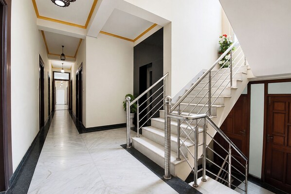 A hallway with a marble floor, a staircase with metal railings, and a wooden door.