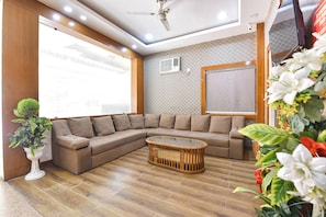 A modern living room with a sectional sofa, a glass coffee table, a ceiling fan, and a large window with blinds.