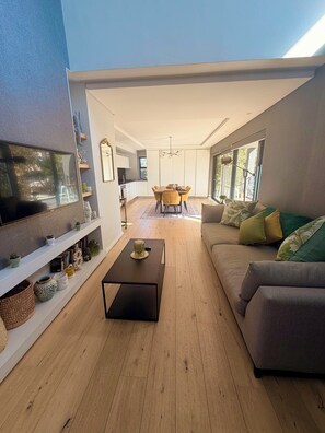 Ein modernes Wohnzimmer mit Flachbildfernseher, Couch, Couchtisch und einem Essbereich mit Tisch und Stühlen.