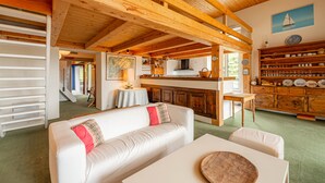 A cozy interior with a wooden ceiling, a white sofa, a dining table, and a kitchen area with wooden cabinets and a view of the outdoors. - SmartStay Planet - Argentière (Argentière)