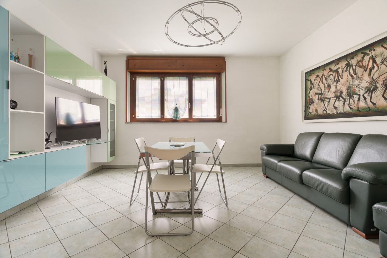 A modern living room with a TV, dining table, chairs, a sofa, and artwork on the wall.