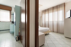 Ein modernes Hotelzimmer mit Bett, kleinem Schreibtisch, Toilette und Duschbereich.
