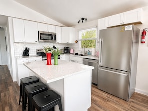 A modern kitchen with white cabinets, stainless steel appliances, and a central island with stools. - "The Creel" 3BR Lakefront, Hot Tub, Resort Access (Lake Harmony)