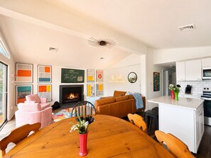 A modern living room with a fireplace, a dining table with chairs, and a kitchen area with white cabinets and a microwave. - "The Creel" 3BR Lakefront, Hot Tub, Resort Access (Lake Harmony)