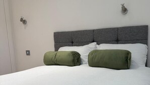 Ein Bett mit grauem Kopfteil, weißer Bettwäsche und zwei grünen Kissen.