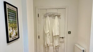 Ein Zimmer mit Holzboden, einer weißen Tür mit Kleiderhaken und einem gerahmten Bild an der Wand.